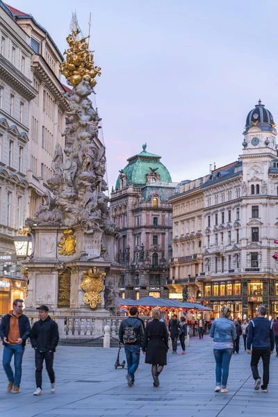 Wenen, Oostenrijk - 28 april 2019: Mensen die over straat lopen die langs de pestzuil in de oude binnenstad lopen — Stockfoto
