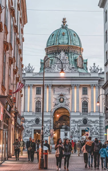 Wien, Österrike - 28 april 2019: Folk går på gatan kohlmarket med utsikt över Hofburg Imperial Palace under solnedgången — Stockfoto