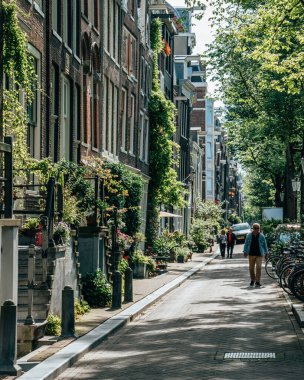 Amsterdam, Hollanda - 21 Temmuz 2019: Yerel halk tembel bir öğleden sonra kanal caddesinde yürüyor