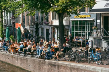 Amsterdam, Hollanda - 21 Temmuz 2019: Dışarıda oturanlar Singel yakınlarındaki kanalda güneşli bir öğleden sonranın tadını çıkarıyorlar