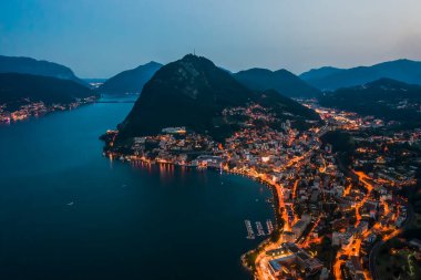 High angle aerial drone night shot of city street lights by lake monte salvatore in Lugano, Switzerland clipart
