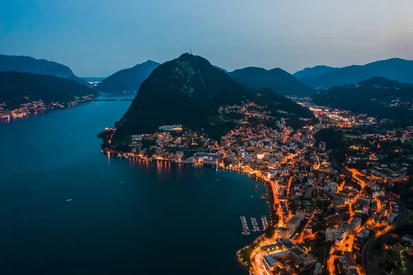 Hoge hoek luchtfoto drone nacht shot van de stad straatverlichting door meer monte salvatore in Lugano, Zwitserland — Stockfoto