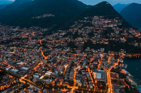 Hoge hoek luchtfoto drone nacht shot van de stad straatverlichting door meer monte salvatore in Lugano, Zwitserland — Stockfoto