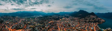 Panorama aerial drone night shot of city street lights by lake in Lugano, Switzerland clipart