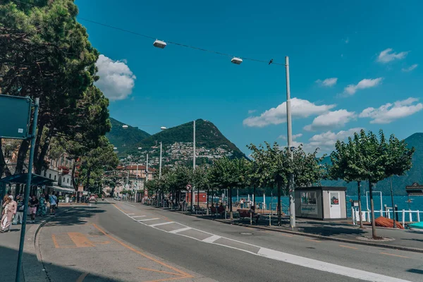 Lugano, Szwajcaria - sierpień4, 2019: Miejska ulica Lugano nad jeziorem z białymi chmurami i Monte Bre w tle — Zdjęcie stockowe