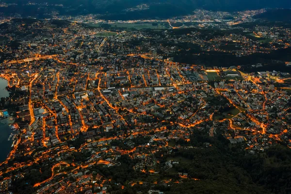 Wysoka kąt lotu drona widok z lotu ptaka Lugano nad jeziorem z miejskich świateł ulicznych po zachodzie słońca w Szwajcarii — Zdjęcie stockowe