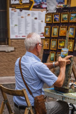 Malcesine, İtalya - 7 Ağustos 2019: Yaşlı adam şehir merkezinde küçük bir formatta resim yapıyor