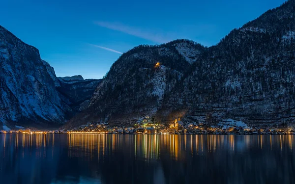 Villaggio nevoso austriaco Hallstatt sul lago circondato da montagne di neve con luci accese dopo il tramonto durante la notte — Foto Stock