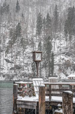 Almanya 'da kış aylarında yoğun kar yağarken Konigssee Gölü' nün yanındaki rıhtımda saat.