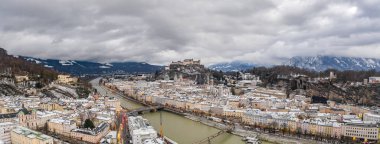 Panoramik hava aracı karlı Salzburg 'un eski kasabasını ve Hohensalzburg kalesini kışın ağır bulutlu tepede görüntüledi.