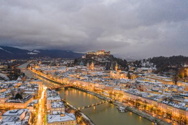 Kışın alacakaranlıkta şehrin ışıklarıyla Salzburg 'un karlı ve eski kasabasının insansız hava aracı görüntüsü.
