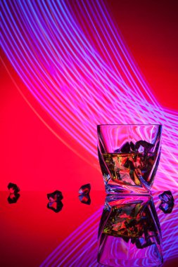 Kokteyl viski parti kavramı mor ışık efektleri kırmızı zemin üzerine bir bardak adet buz ile.