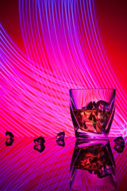 Kokteyl viski parti kavramı mor ışık efektleri kırmızı zemin üzerine bir bardak adet buz ile.