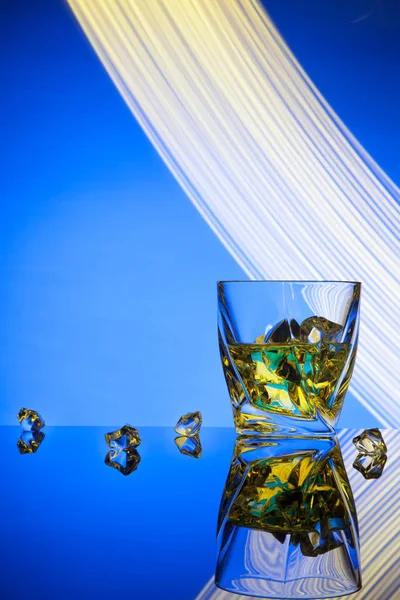 Cocktail whisky een glas met stukken ijs partij concept lichteffecten op blauwe achtergrond. — Stockfoto