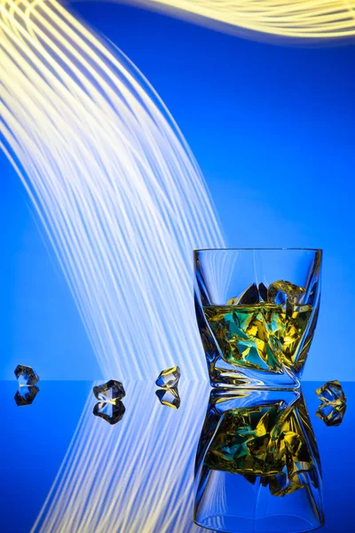 Whisky cocktail un bicchiere con pezzi ghiaccio del concetto di partito effetti di luce su sfondo blu . — Foto Stock