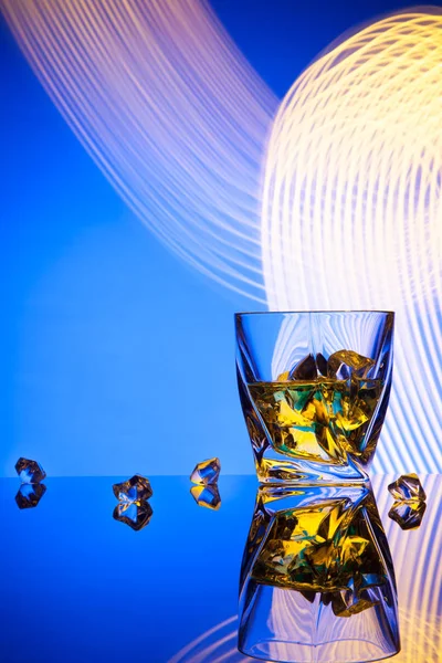 Whisky cóctel un vaso con trozos de hielo de fiesta concepto efectos de luz sobre fondo azul . — Foto de Stock