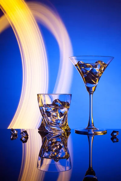 Twee brillen een cocktail Martini whisky ice, tegen de blauwe achtergrond van prachtige lichteffecten. — Stockfoto