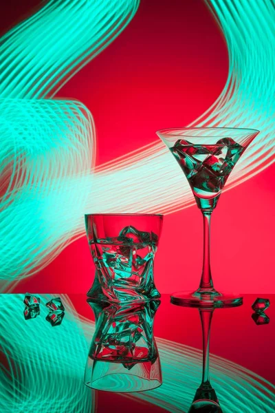 Twee brillen een cocktail Martini whisky ice, tegen de rode achtergrond van prachtige lichteffecten. — Stockfoto