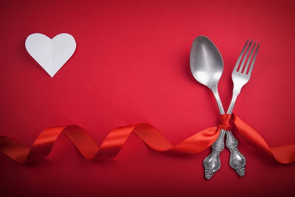 Cuchara y tenedor vintage con una cinta roja y corazón blanco para el día de San Valentín sobre un fondo rojo . —  Fotos de Stock