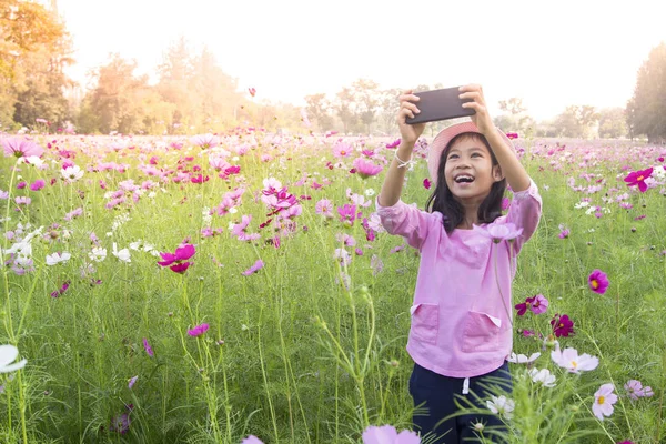 Pouco asiático menina no cosmos flor celular câmera tirar fotos — Fotografia de Stock