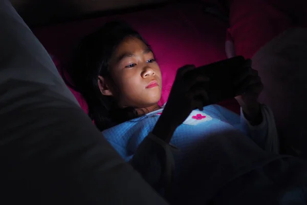 Gadis menggunakan ponsel di tempat tidur gelap di kamar tidur — Stok Foto