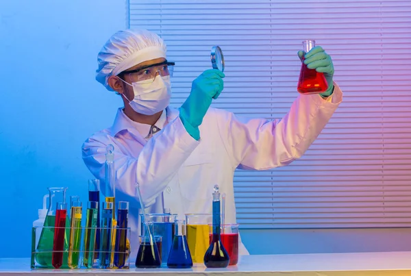 Man scientist holding a test tube with magnifying glass — Stock Photo, Image