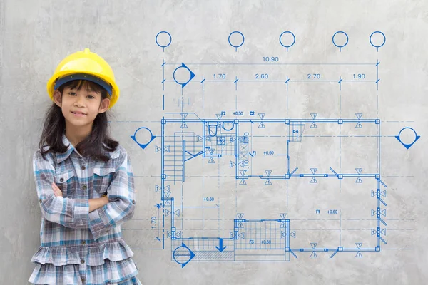 Smiling little girl in yellow helmet showing blueprint drawing on wall — Stock Photo, Image