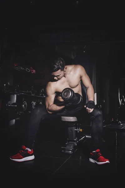 Азиатский юноша с гантелями, напрягающий мышцы в спортзале — стоковое фото