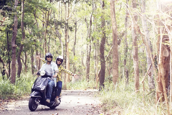 Beau jeune couple dans des casques chevauchant un scooter à travers la forêt — Photo