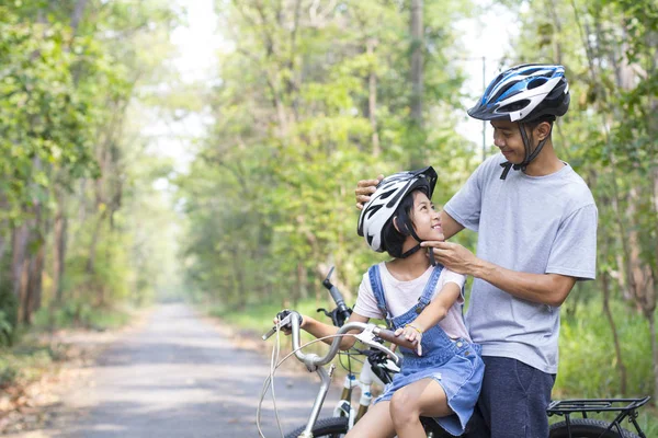 Happy father and daughter cycling in the park wears a bicycle helmet to his daughter