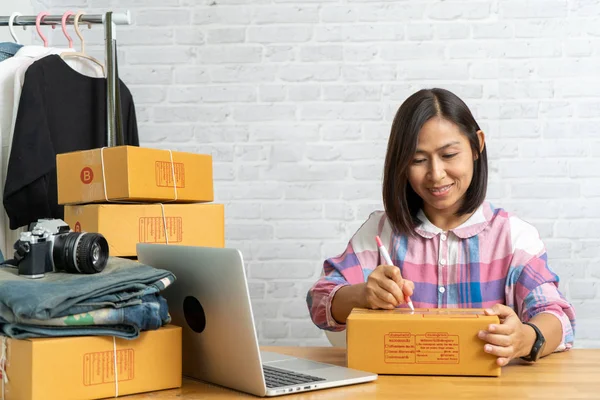 オンライン販売アジアの女性は、自宅のオフィスで郵便小包に書き込みアドレスで、中小企業の所有者の作業を開始します — ストック写真