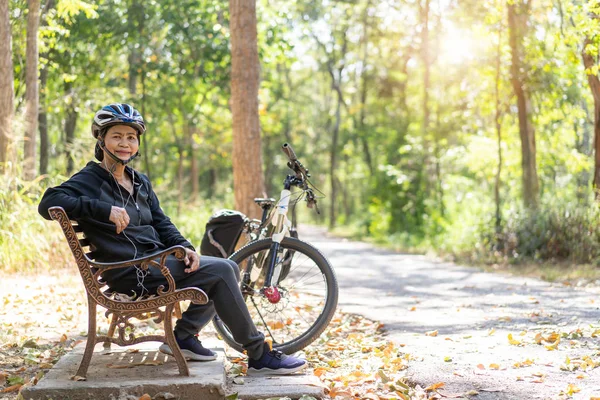 Sênior asiático mulher bicicleta com sentado no parque, com o uso — Fotografia de Stock