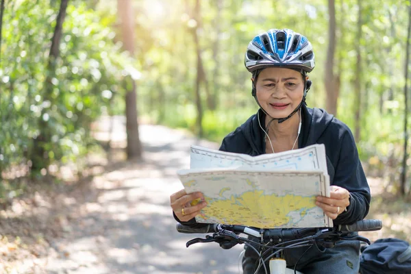 Senior asiatico donna equitazione biciclette in parco con hold e guarda mappa o — Foto Stock