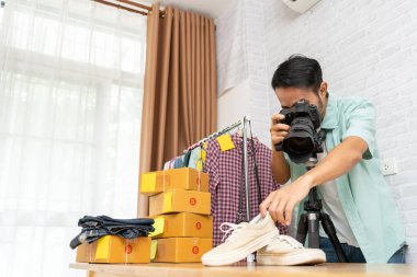 İnternette satışa çıkarmak için dijital kameralı ayakkabılara fotoğraf çeken Asyalı bir adam ev ofisinde küçük işletme sahibi e-ticaret kuruyor.