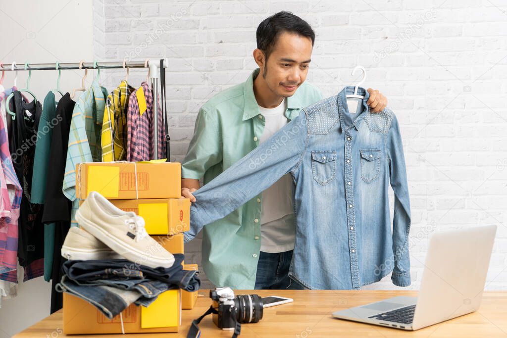 Asian man using computer laptop selling online denim shirt, Start up small business owner e-commerce working at home office