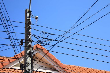 Mavi gökyüzünde elektrik direği ve kablo, arka plandaki evin çatısı.