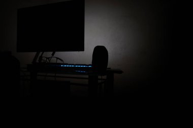 Karanlık odadaki bilgisayarın arka görüntüsü mavi tuşlu ve gözlüklü ve hoparlörlü, insan yok, resme odaklı değil