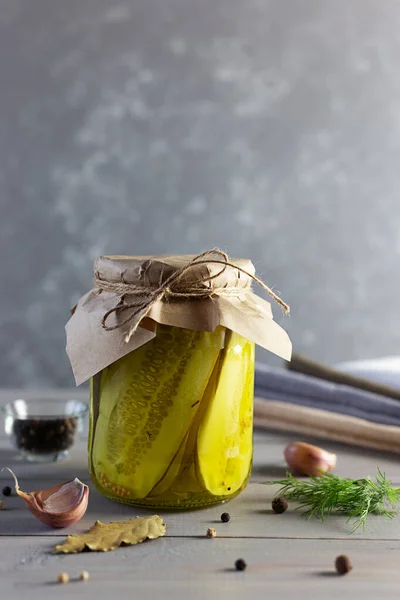 Pickled fermented cucumbers in a glass jar. Pickles with garlic, pepper and dill on a gray wooden background.