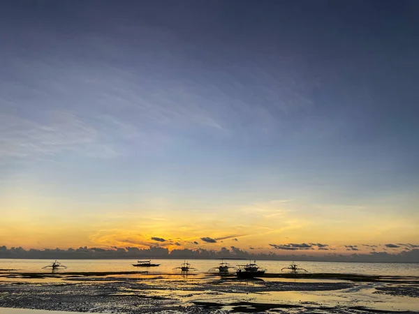 İnanılmaz güzel bir gün batımı, turuncu gölgeli tropiklerde gün doğumu, tekneli deniz, kumlu sahilde alçak dalga.