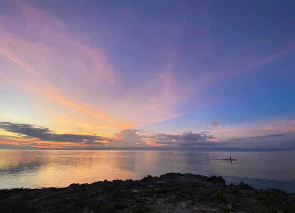 İnanılmaz güzel gün batımının büyülü manzarası, şafak. Denizde kayıkla giden bir adam. Ufukta mavi gökyüzü ve renkli bulutlar. Kaya kıyısı.