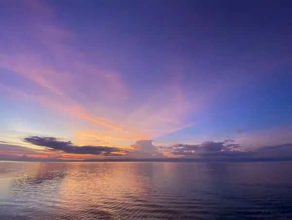 Renkli güzel gün batımı, pembe, mor, mavi tonlarıyla şafak. Sudaki bulutların yansımasıyla sakin bir deniz..