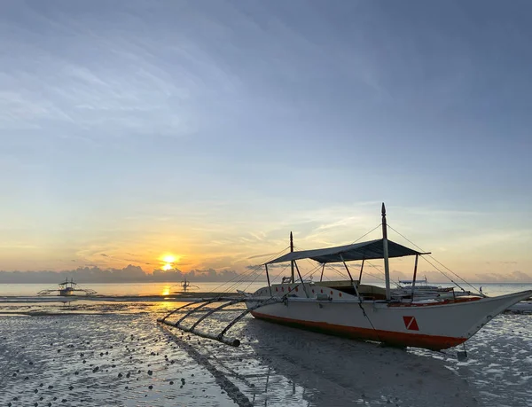 Tekne yakın plan. Güzel sarı-turuncu gün batımı, şafak vakti gökyüzü arkasında. Küçük taşlarla kumlu bir sahilde alçak gelgit.