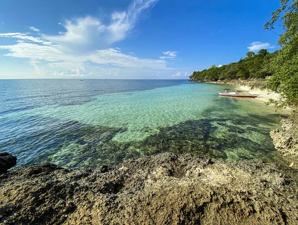 Kayalık bir sahilin inanılmaz güzel manzarası şeffaf bir turkuaz deniz ve beyaz bulutlu mavi bir gökyüzü. Ağaçların yakınındaki kumsalın kıyısında bir tekne..