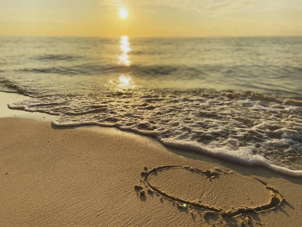 Okyanus arka planında kumlu bir sahilde inanılmaz güzel bir günbatımının, güneşin doğuşunun kalbi çizildi. Bir deniz dalgasının beyaz köpüğü.