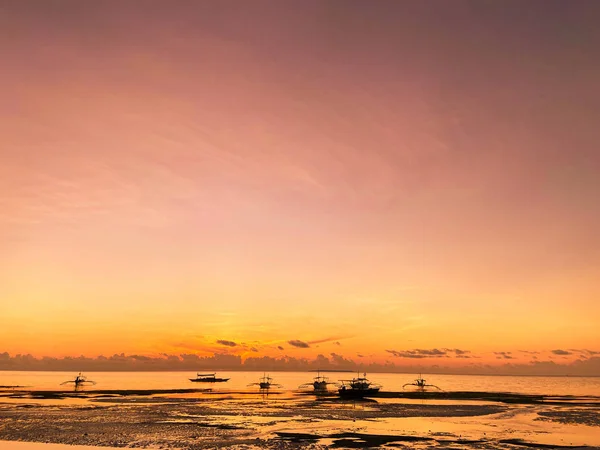 İnanılmaz güzel, sihirli kırmızı gün batımı, tropiklerde gün doğumu, gölgeli. Ufukta kara siluetleri olan sakin bir deniz. Arka planda gökyüzü ve bulutlar. Kumlu bir sahilde gelgit var..