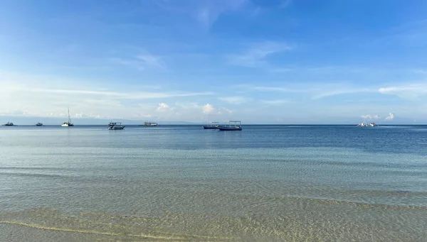 Tek renkli güzel mavi gökyüzü ve sakin deniz manzarası. Ufukta gemiler ve gemiler okyanusta sürükleniyor. Şeffaf sığ su, alçak gelgit.