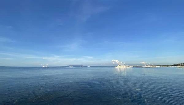 Mavi gökyüzü ve sakin denizin güzel tek renkli manzarası. Bir gemi ve kayıklar ufukta süzülüyor.