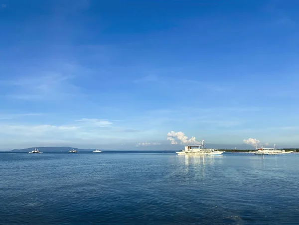 Tek renkli güzel mavi gökyüzü ve sakin deniz manzarası. Ufukta okyanusta beyaz bulutların arkasında gemiler ve gemiler sürükleniyor.