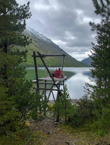Sevgi dolu bir çift, sırtı ekoseli bir adam göle, dağlara bakar.