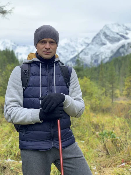 Guide man holds stick in his hands,at background the backdrop of snow mountains